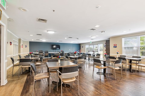 A large room with tables and chairs and a TV on the wall.
