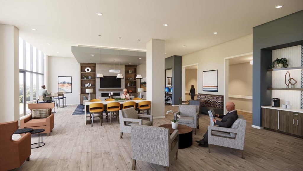 A man in a suit is sitting in a grey armchair in a spacious room with a wooden floor and a large window.