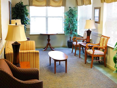 A living room with a brown chair, a brown ottoman, a brown armchair, a wooden table, and a lamp.