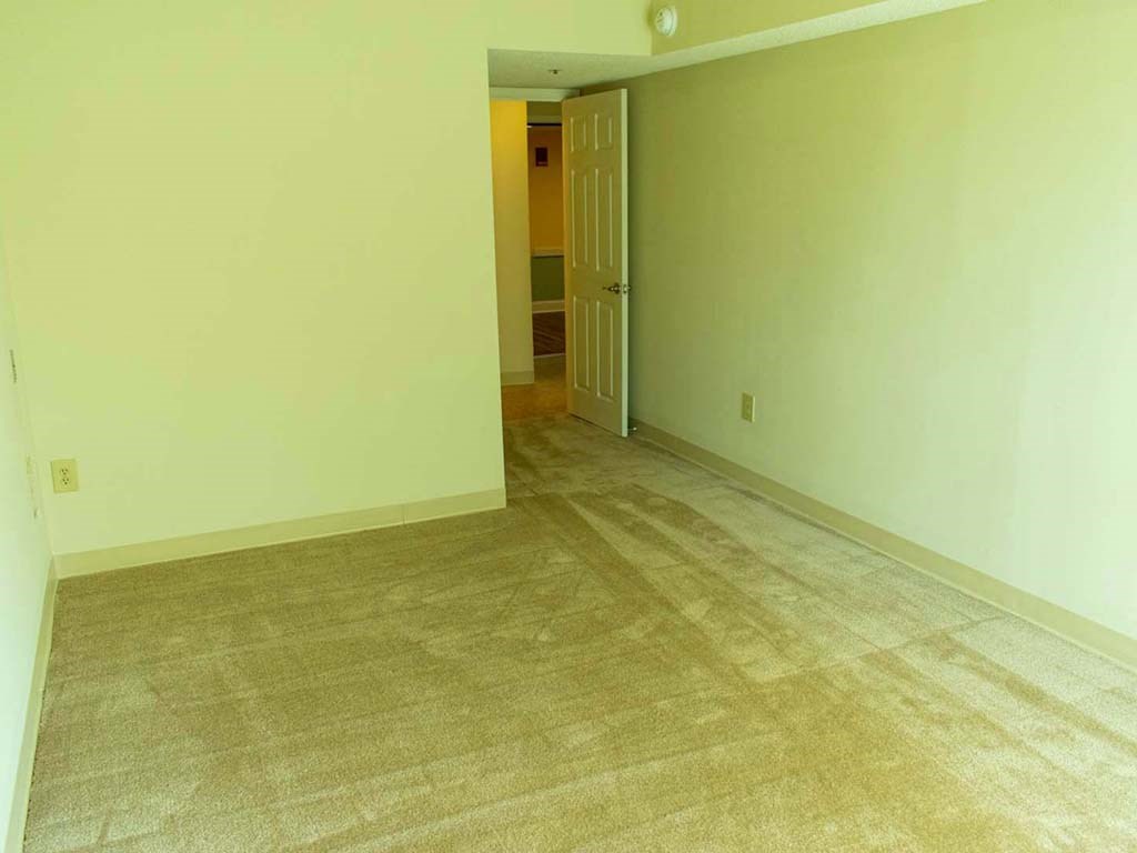 an empty living room with carpet and a door to a hallway
