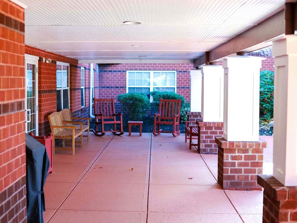 a porch with chairs and a table in front of a brick building