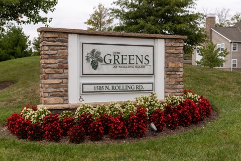 A sign for The Greens at Rolling Road stands in front of a house.