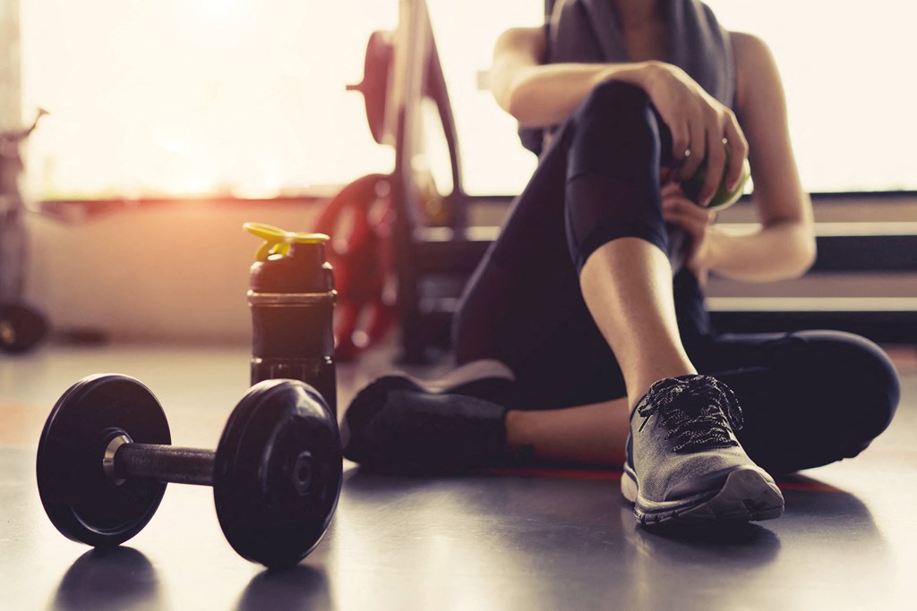 a woman sitting on the floor next to a dumbbell and a drink