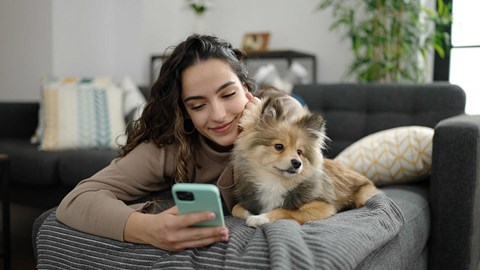 a woman laying on a couch holding a dog and looking at her cell phone