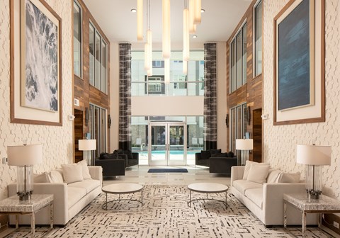A large, modern living room with a white sofa set and a patterned rug.