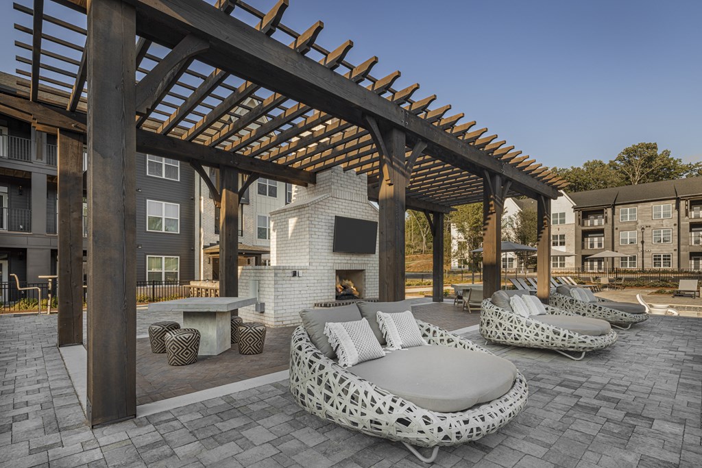 A wooden pergola over a patio with white cushioned seating at Folksong Apartments, Flowery Branch, GA