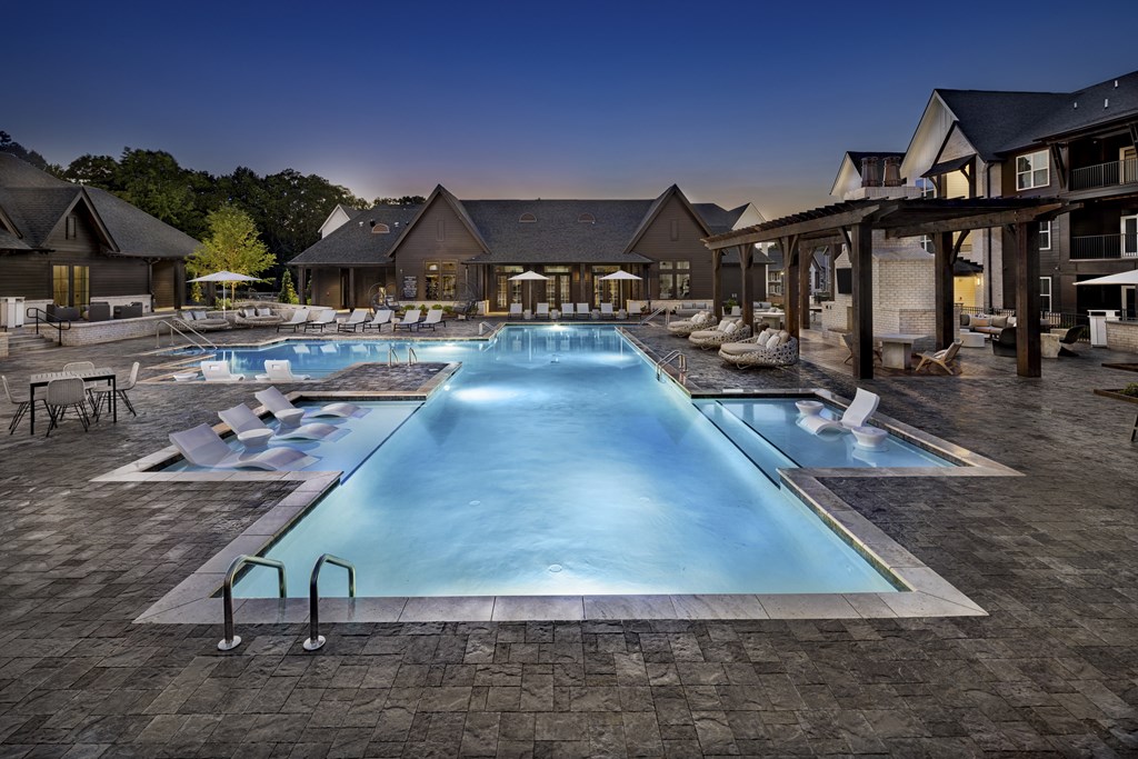 A large swimming pool surrounded by a patio area with chairs and a building in the background at Folksong Apartments, Georgia 30542