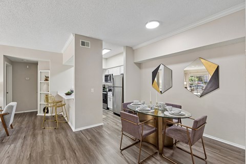 A dining room with a table set for two and a kitchen in the background.