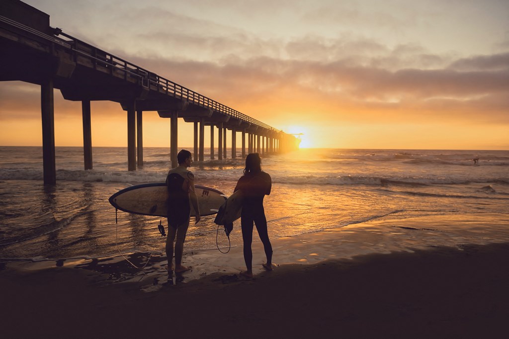 two people standing on the beach with surfboards at sunset