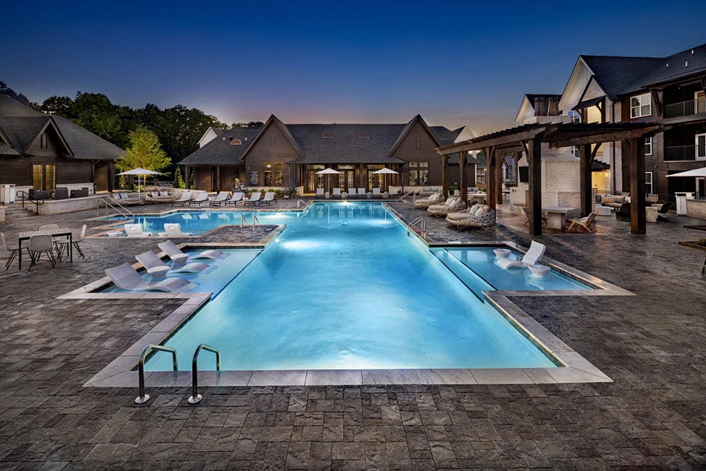 A large swimming pool surrounded by a patio area with chairs and a building in the background.