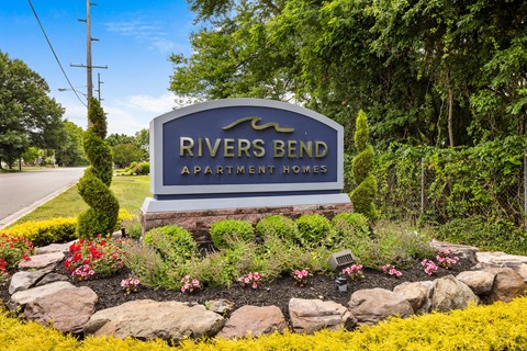 A sign for Rivers Bend Apartment Homes is surrounded by flowers and greenery.