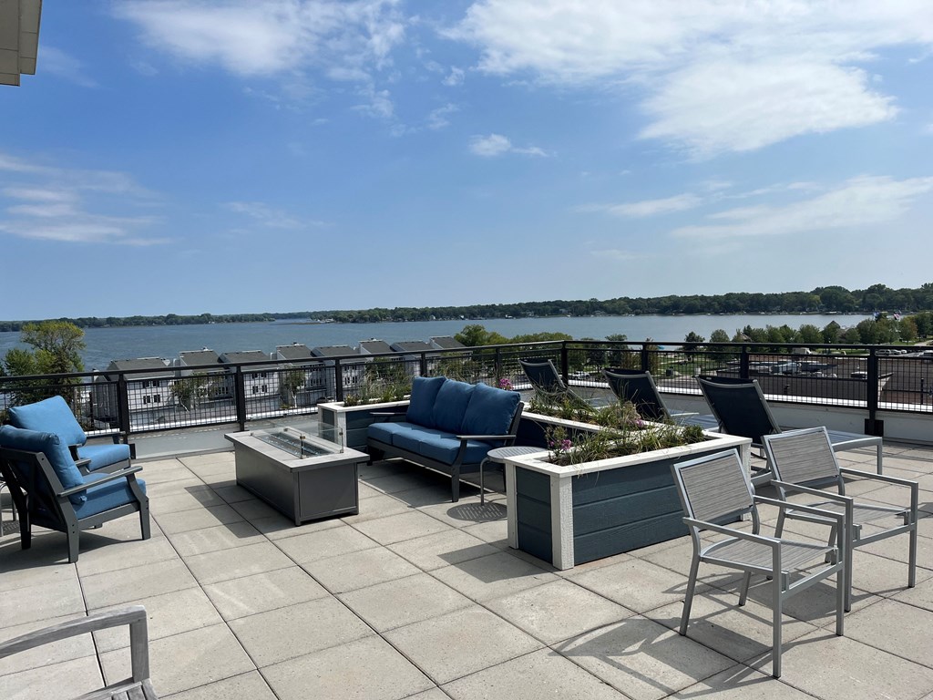 a rooftop patio with chairs and tables and a river in the background