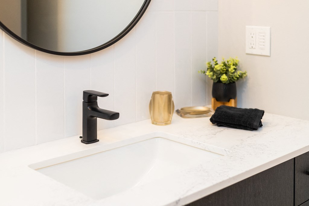 a white bathroom sink with a black faucet and a black mirror