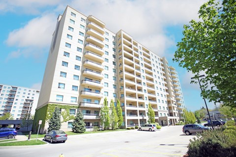 A large white apartment building with balconies and a parking lot in front.