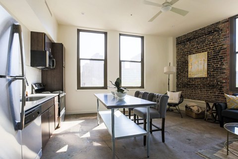 A kitchen with a refrigerator, a dining table with chairs, and a brick wall.