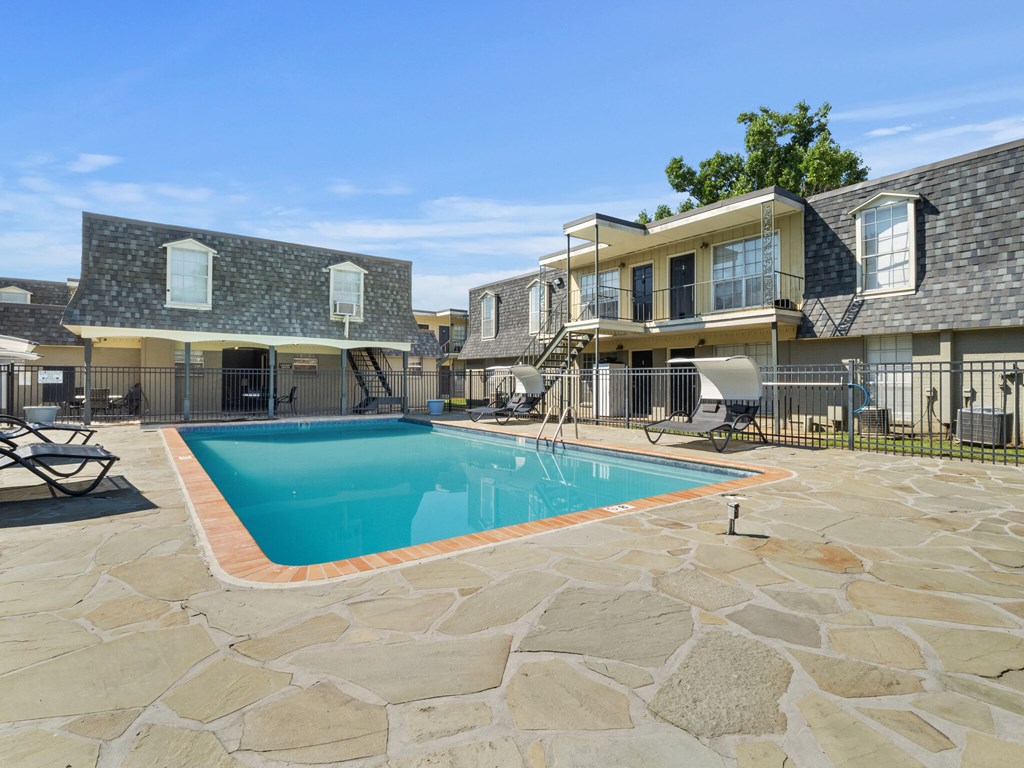 A swimming pool surrounded by stone and a patio area with chairs.