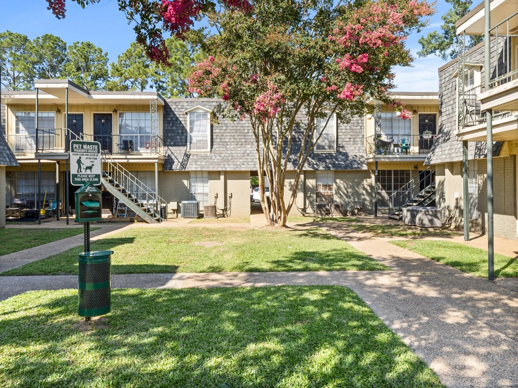 A sunny day at a residential complex with a green lawn and a dog park sign.