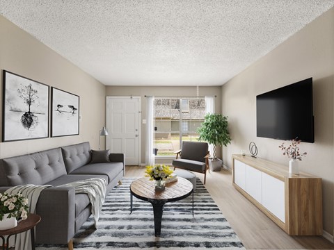A living room with a grey couch, a coffee table, a chair, a plant, and a flat screen TV mounted on the wall.