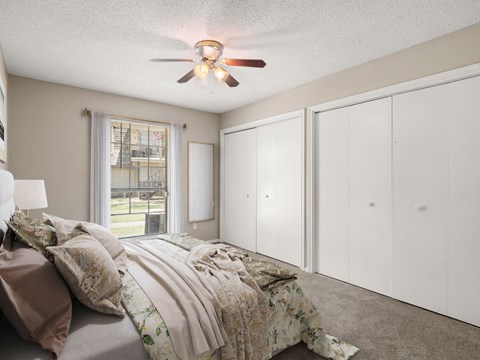 A bedroom with a bed, a ceiling fan, and a window with a view of a fence and trees.
