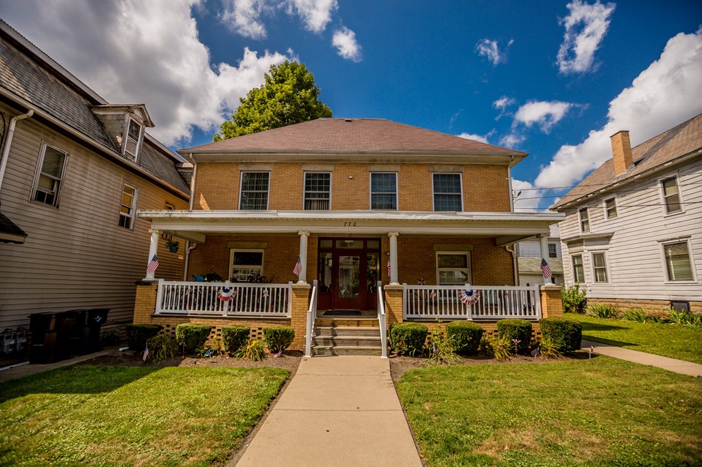 the front of a brick house with a porch and a sidewalk