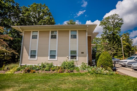 a tan house with a lawn in front of a parking lot