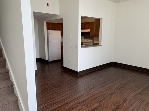 an empty living room with wood flooring and a kitchen