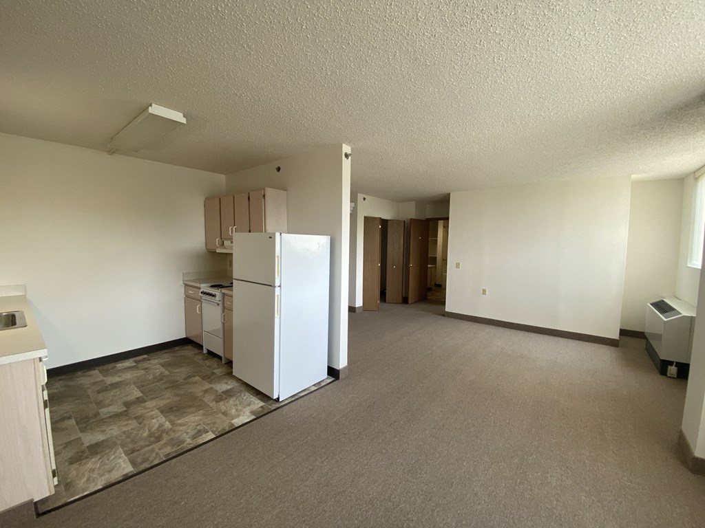 an empty living room with a kitchen and a refrigerator