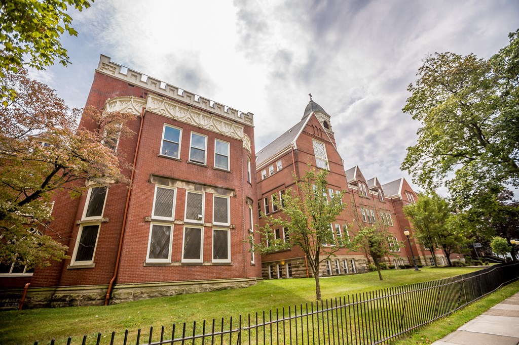 a large brick building with a green lawn and a fence
