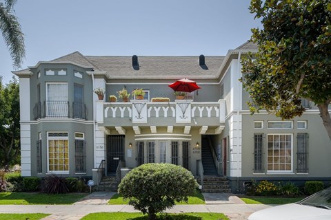 A grey two-story house with a red umbrella on the balcony.