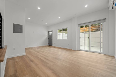 A spacious room with wooden flooring and a sliding glass door.
