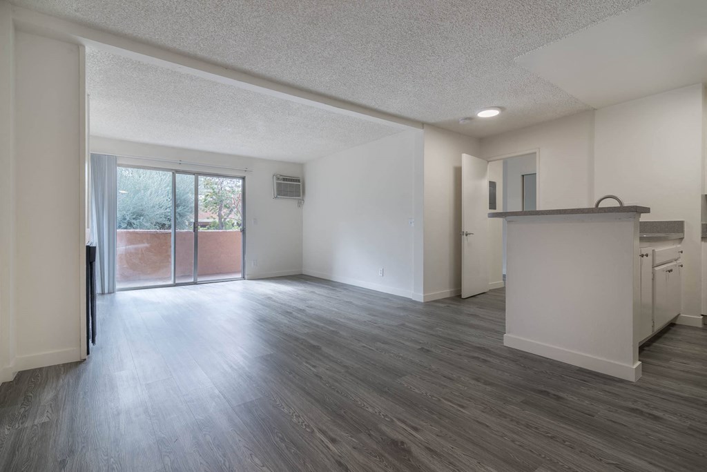 an empty living room with a kitchen and a sliding glass door