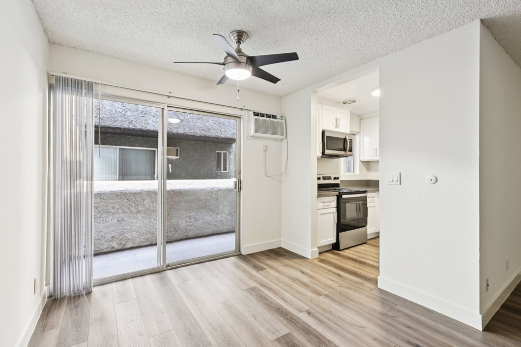 A room with a ceiling fan and a view of a backyard through a sliding glass door.