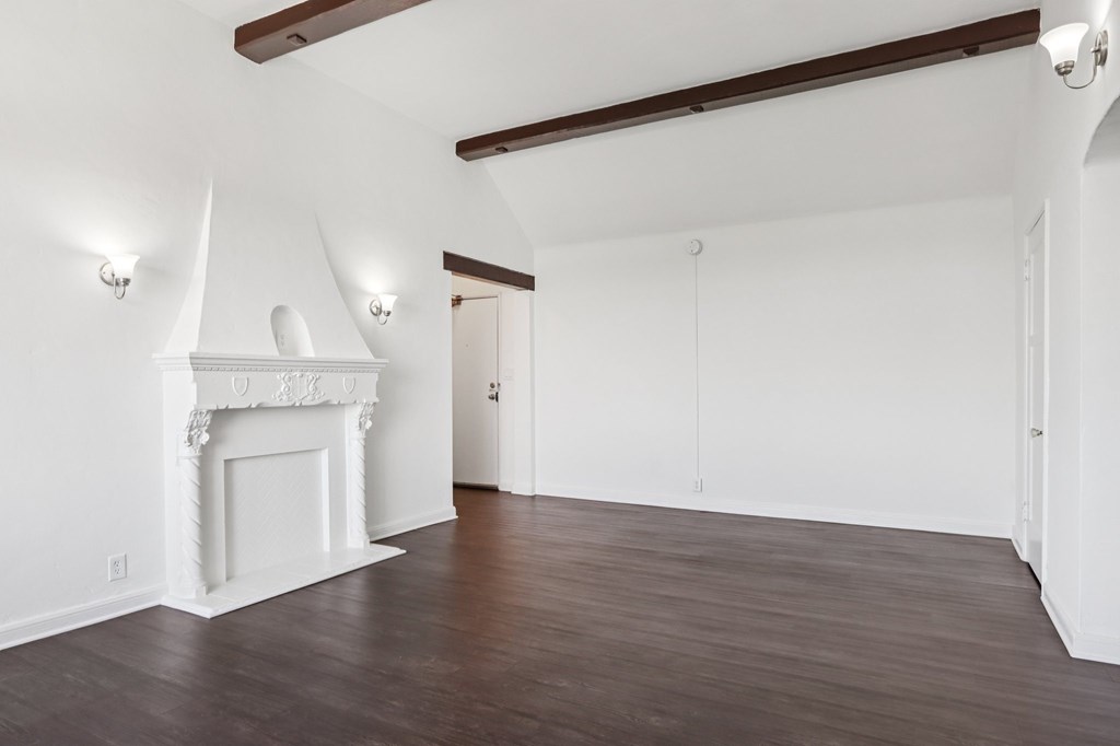 A room with a white fireplace and wooden beams on the ceiling.
