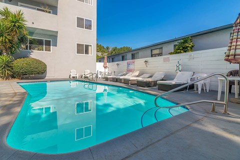 A swimming pool in front of a building with sun loungers.