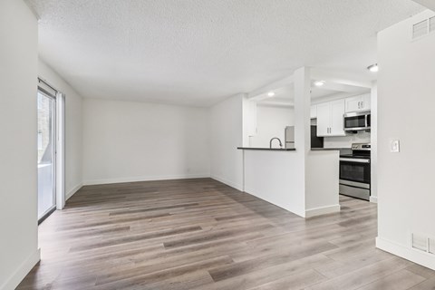 A spacious room with wooden flooring and a kitchen area in the background.