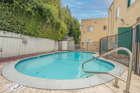 A small pool surrounded by a fence and a wall covered in greenery.