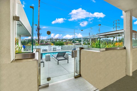 A balcony with a glass door and a bench overlooking a pool.