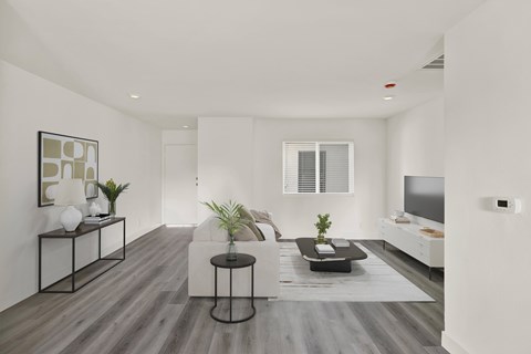 A modern living room with a white couch, a black coffee table, and a TV on the wall.