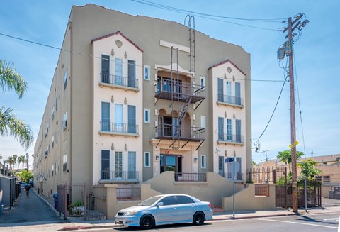 A white car is parked in front of a two-story building with a balcony.