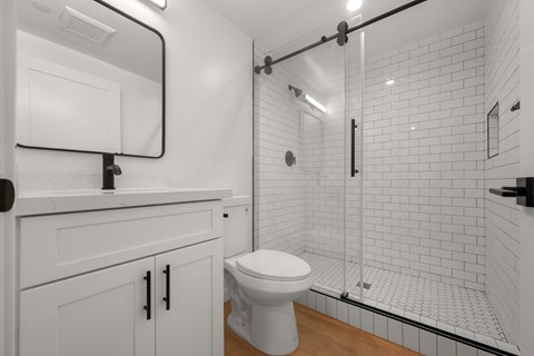 A white toilet sits in a bathroom with a walk-in shower.