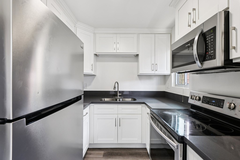 A modern kitchen with a stainless steel refrigerator and black countertops.