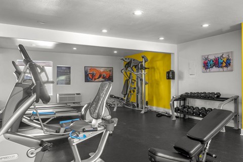 A gym with a rowing machine, a bench press, and a yellow wall.