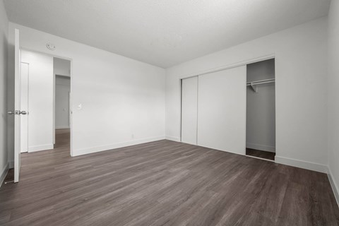 A room with white walls and wood flooring with a door on the left and a closet on the right.