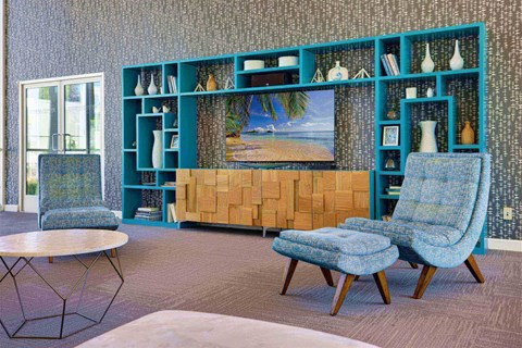 A living room with a blue chair and a painting of a beach on the wall.