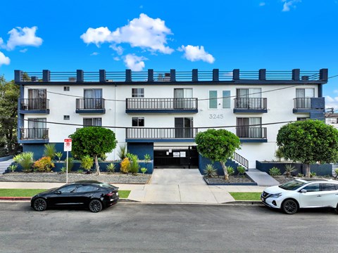 A black car is parked in front of a white building with the number 3245 on it.