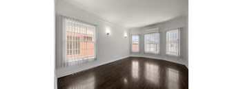 A room with wooden floors and three windows with blinds.