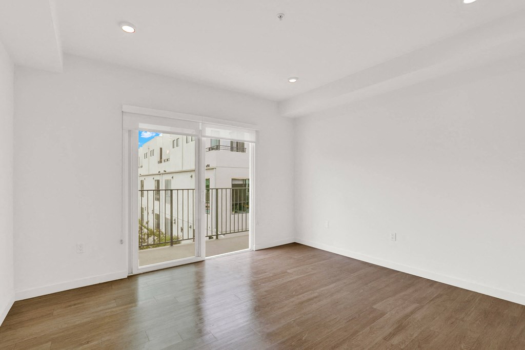 a living room with white walls and a sliding glass door to a balcony