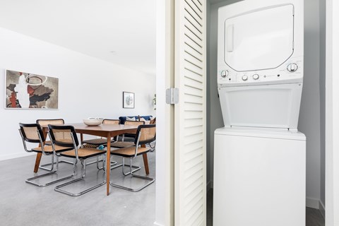 A white washing machine is in a room with a table and chairs.