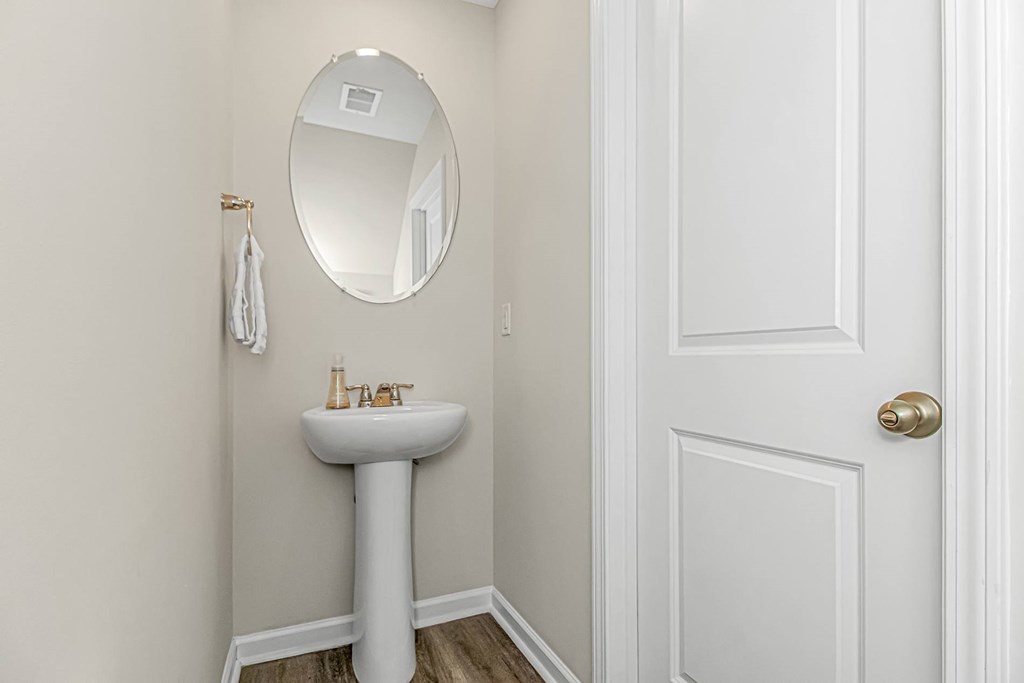 A white pedestal sink with a round mirror above it.