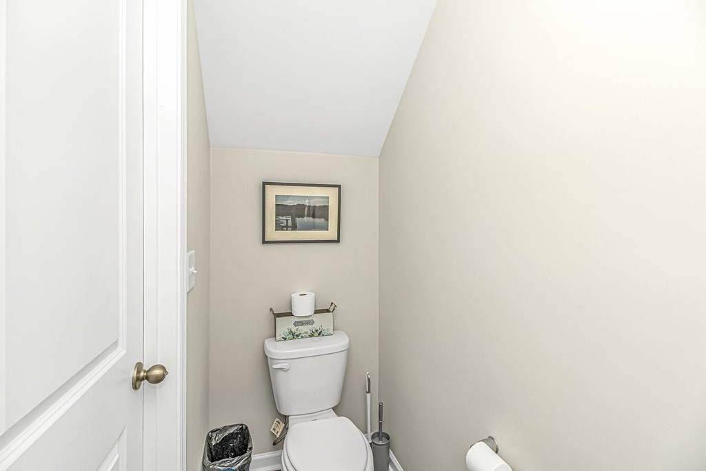 A white toilet in a small bathroom with a picture frame on the wall.